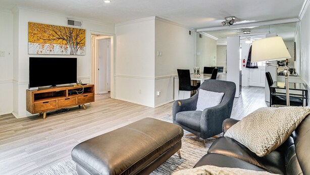 A living room with a flat-screen TV, leather ottoman, and grey armchair. - Condo 9 Mi to Dtwn Dallas: BBQ By the Pool! (Dallas)