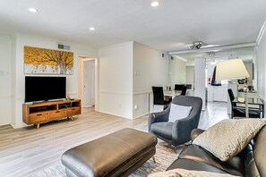 A living room with a flat-screen TV, leather ottoman, and grey armchair. - Condo 9 Mi to Dtwn Dallas: BBQ By the Pool! (Dallas)