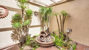 Un patio con cactus, palmeras y una fuente de piedra decorativa.