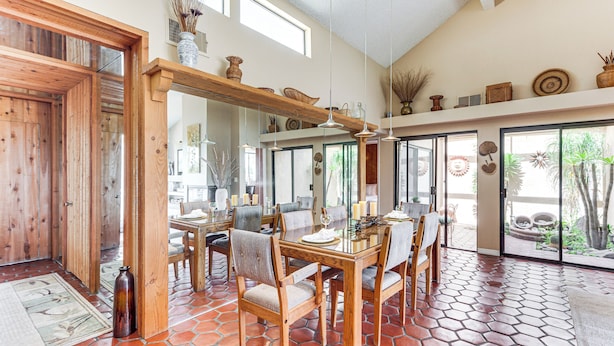 Un comedor con mesa y sillas de madera, piso de baldosas y un ventanal con vistas a la vegetación.