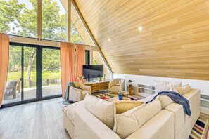 A spacious living room with a large sofa, a television, and a wooden ceiling. - A-frame Cabin w/ Deck Near Cedar Creek Lake (Malakoff)
