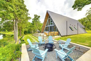 A modern house with a sloped roof, a deck with outdoor furniture, and a fire pit surrounded by Adirondack chairs. - A-frame Cabin w/ Deck Near Cedar Creek Lake (Malakoff)