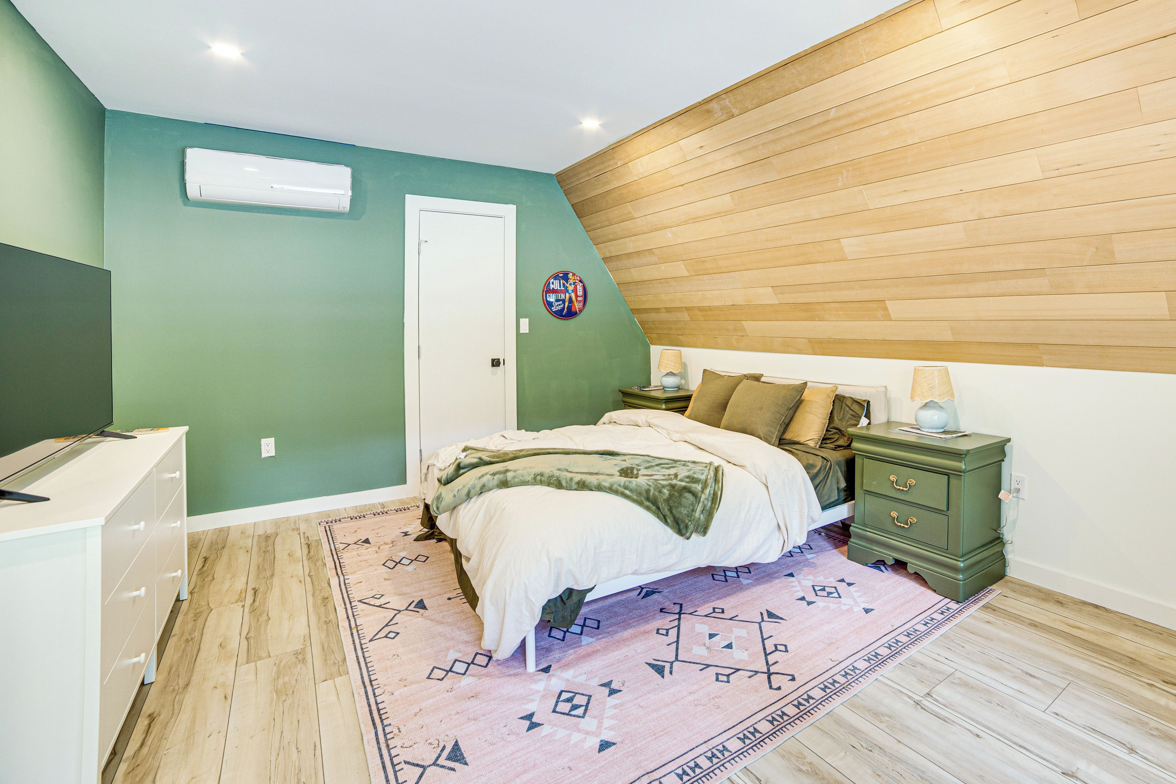 A bedroom with a bed, bedside table, nightstand, and a wall-mounted air conditioner.