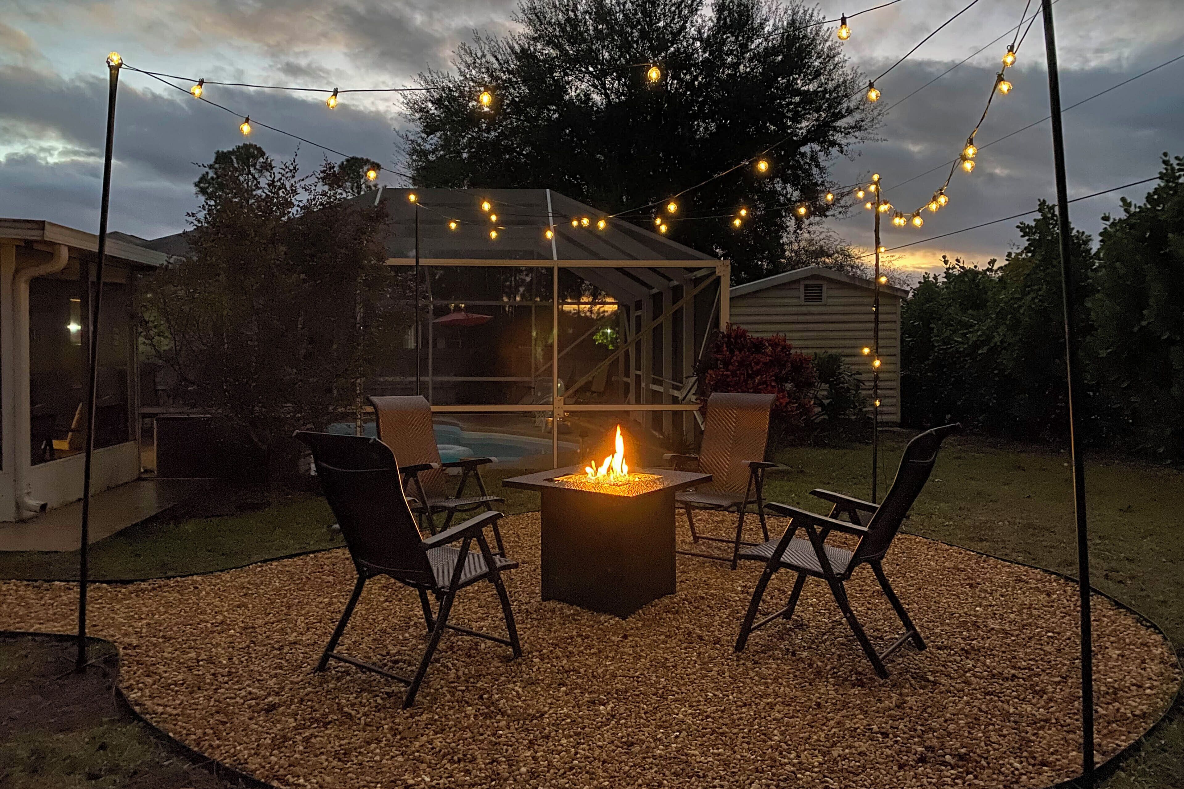 An outdoor patio area with a fire pit, chairs, and string lights.