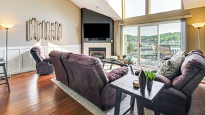 Un salón moderno con chimenea, televisor grande y vistas a un balcón con mobiliario exterior.