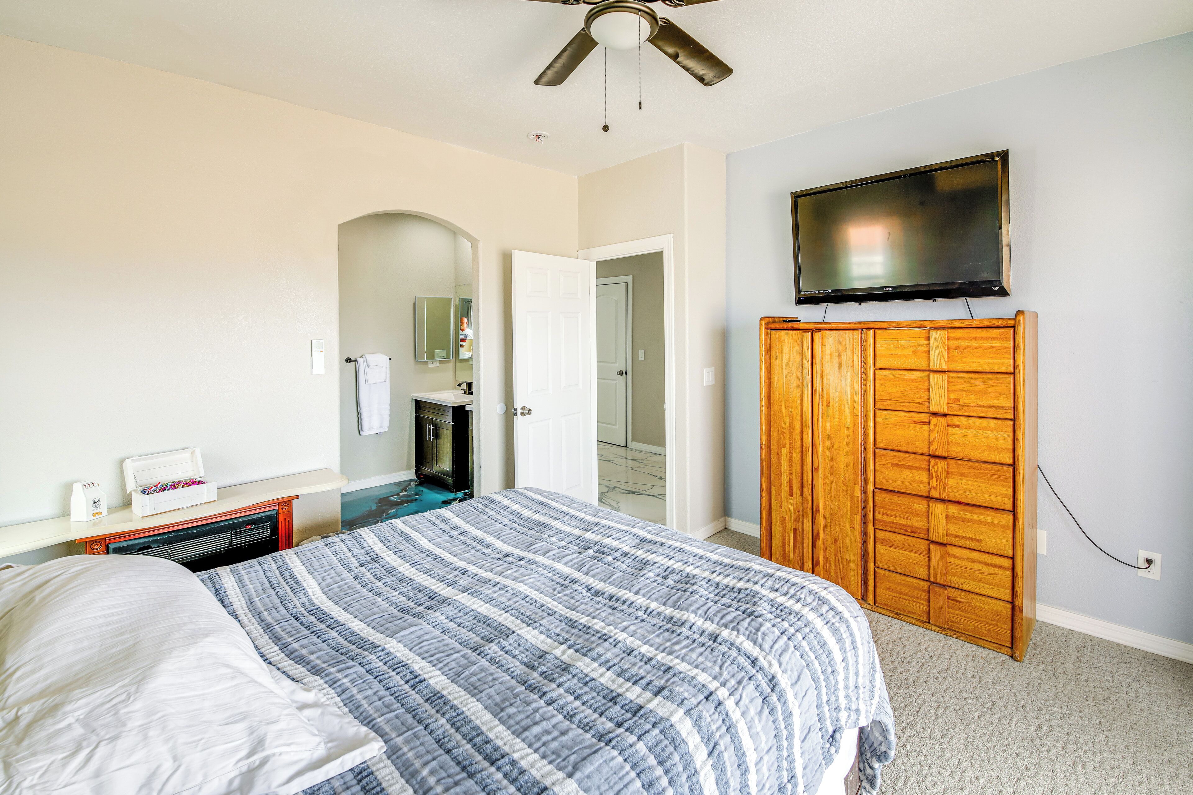 A bedroom with a bed, a wooden wardrobe, a television, and a bathroom visible through an archway.