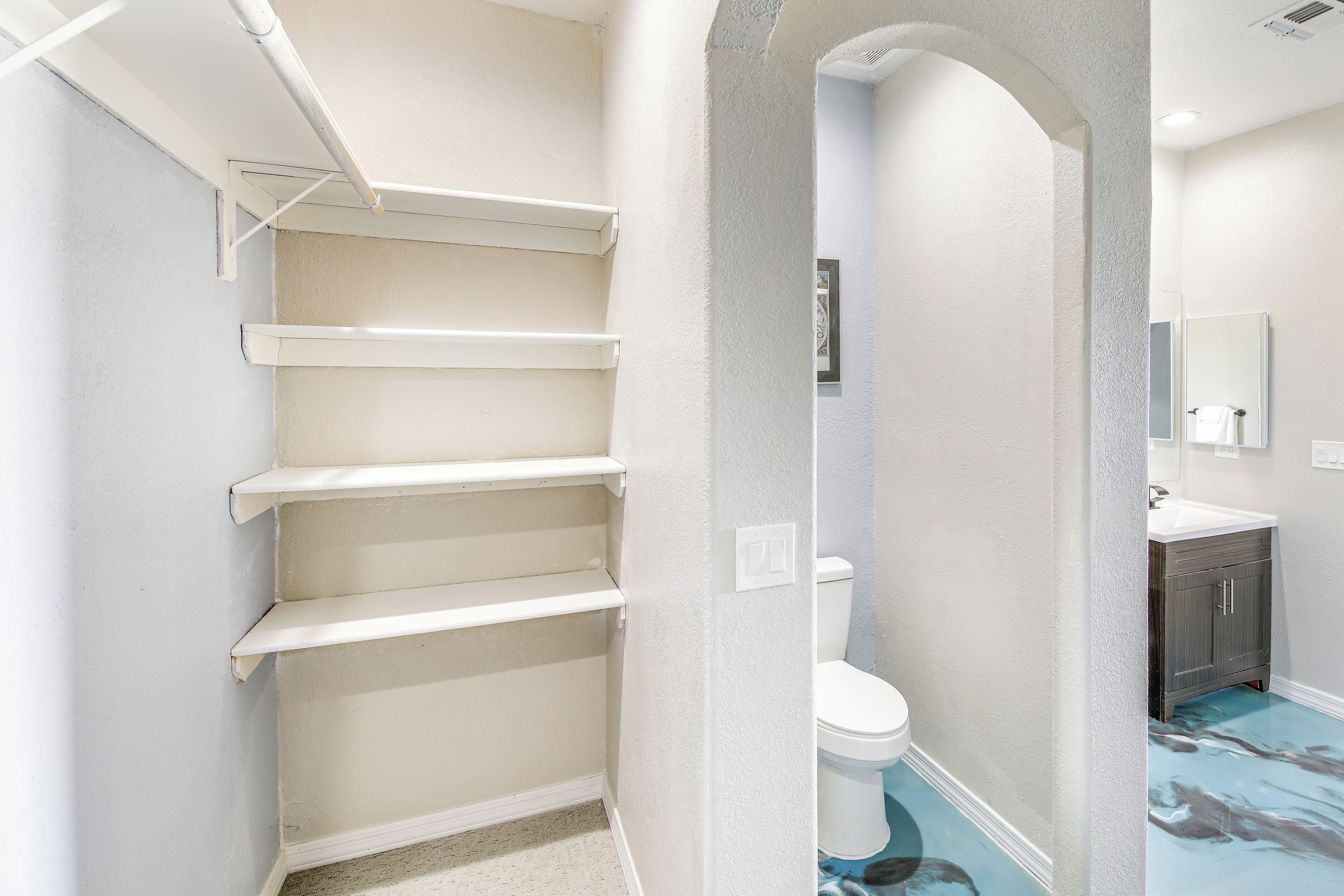 Une salle de bain aux murs blancs, avec des toilettes, un meuble-lavabo doté d’un miroir et un carrelage bleu.