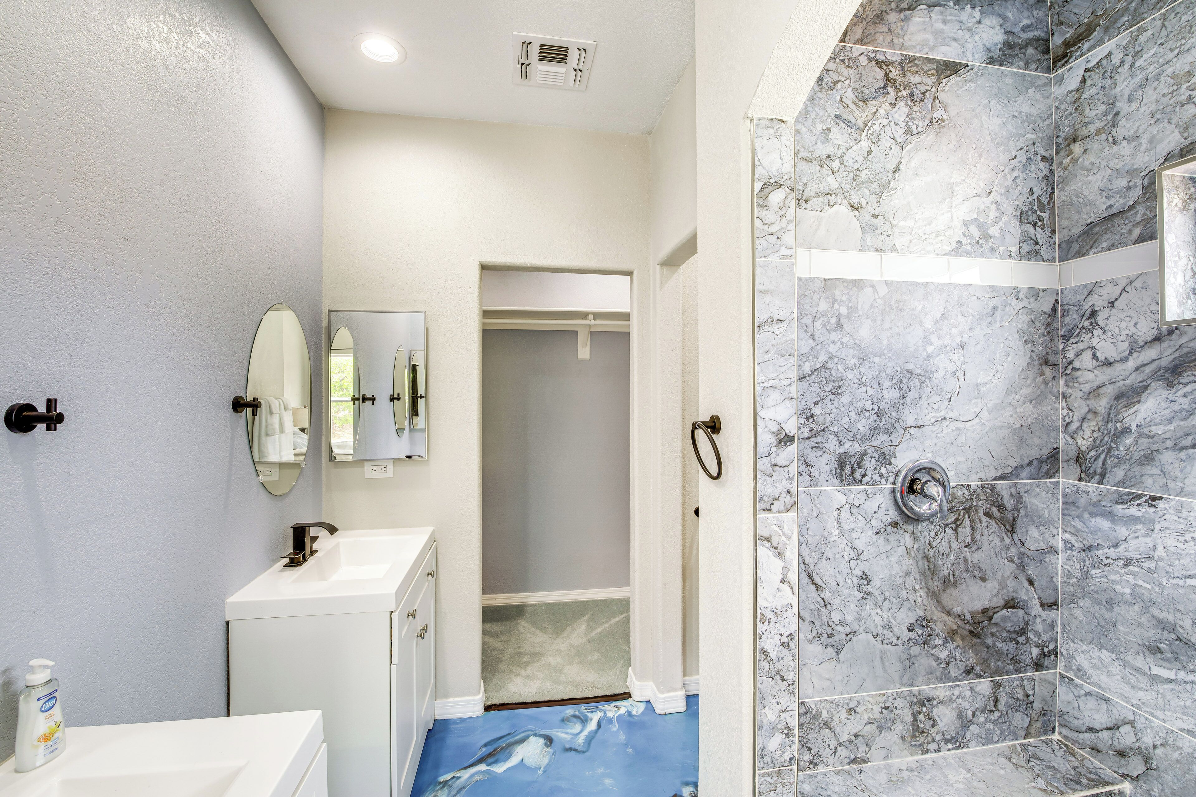 Un baño con ducha de mármol, lavabo blanco y espejo.