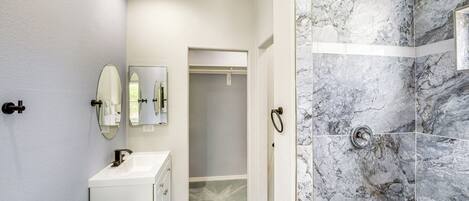 Un baño con ducha de mármol, lavabo blanco y espejo.