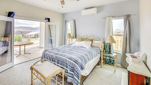 Ein Schlafzimmer mit Bett, Stuhl, Nachttisch, einem Fenster mit Vorhängen, Deckenventilator und Blick ins Freie.