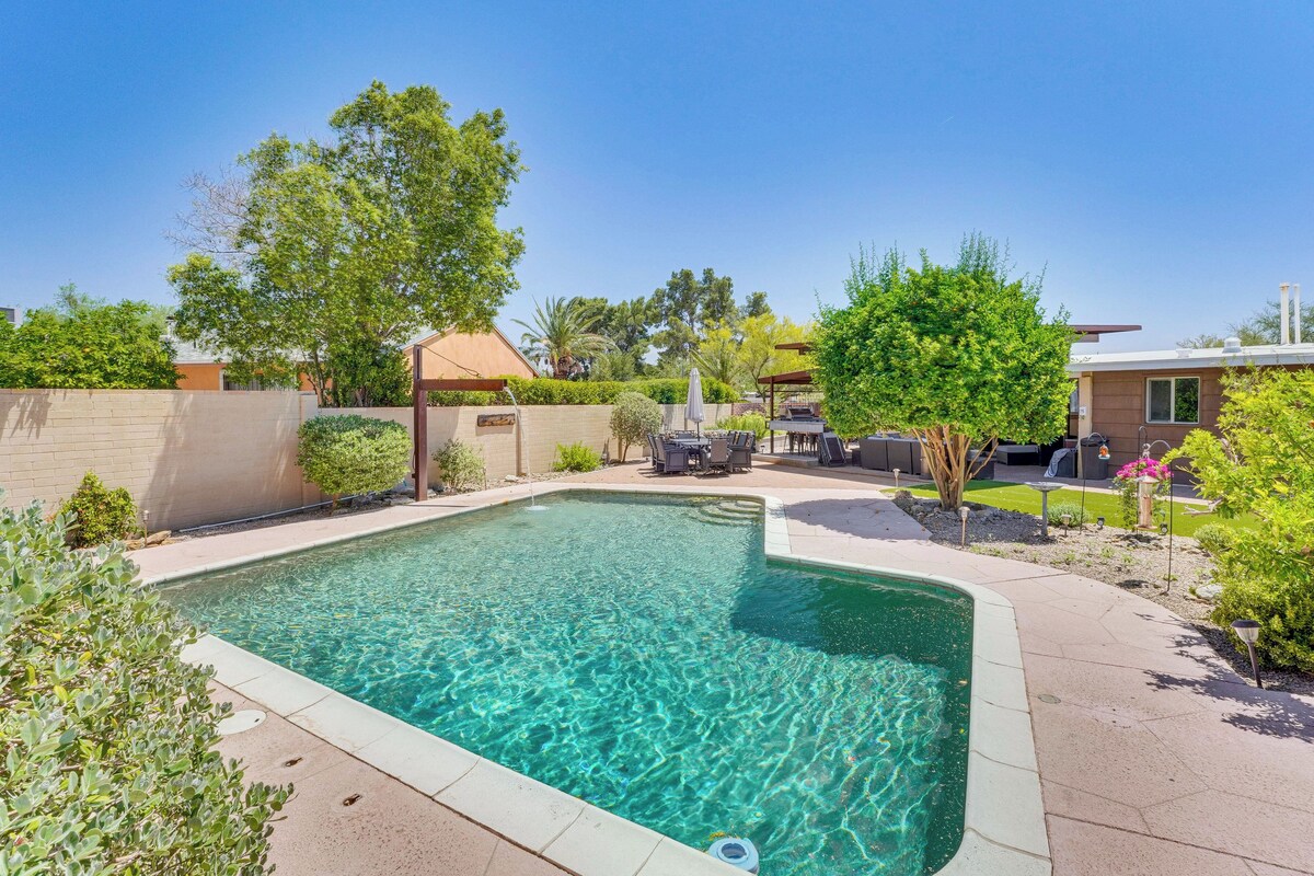 A rectangular swimming pool with clear water, surrounded by a landscaped garden with various plants and trees.