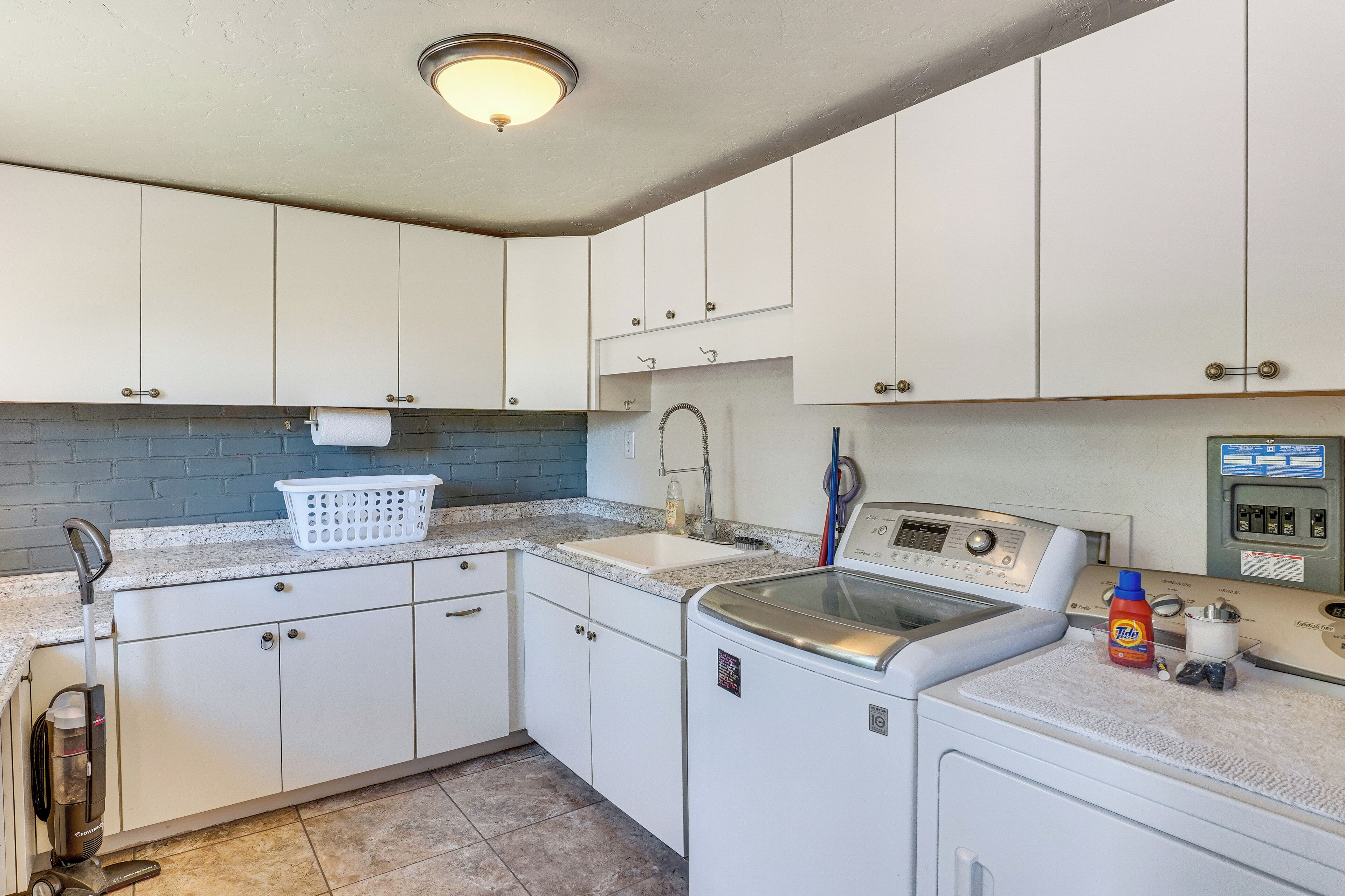 A laundry room with a washing machine, dryer, sink, and a vacuum cleaner.