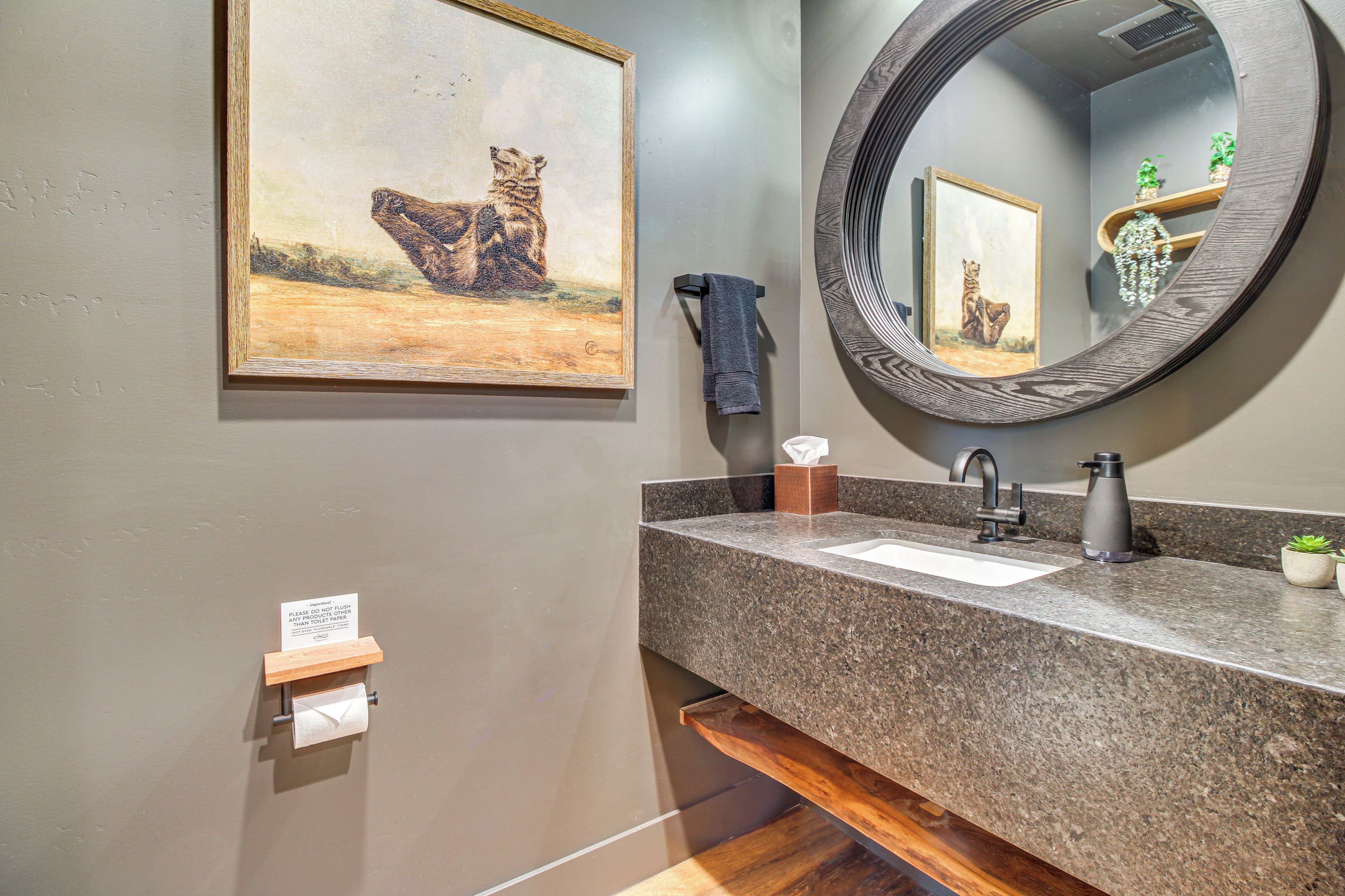 A bathroom with a granite countertop, a sink, a mirror, a towel rack, and a painting of a bear.