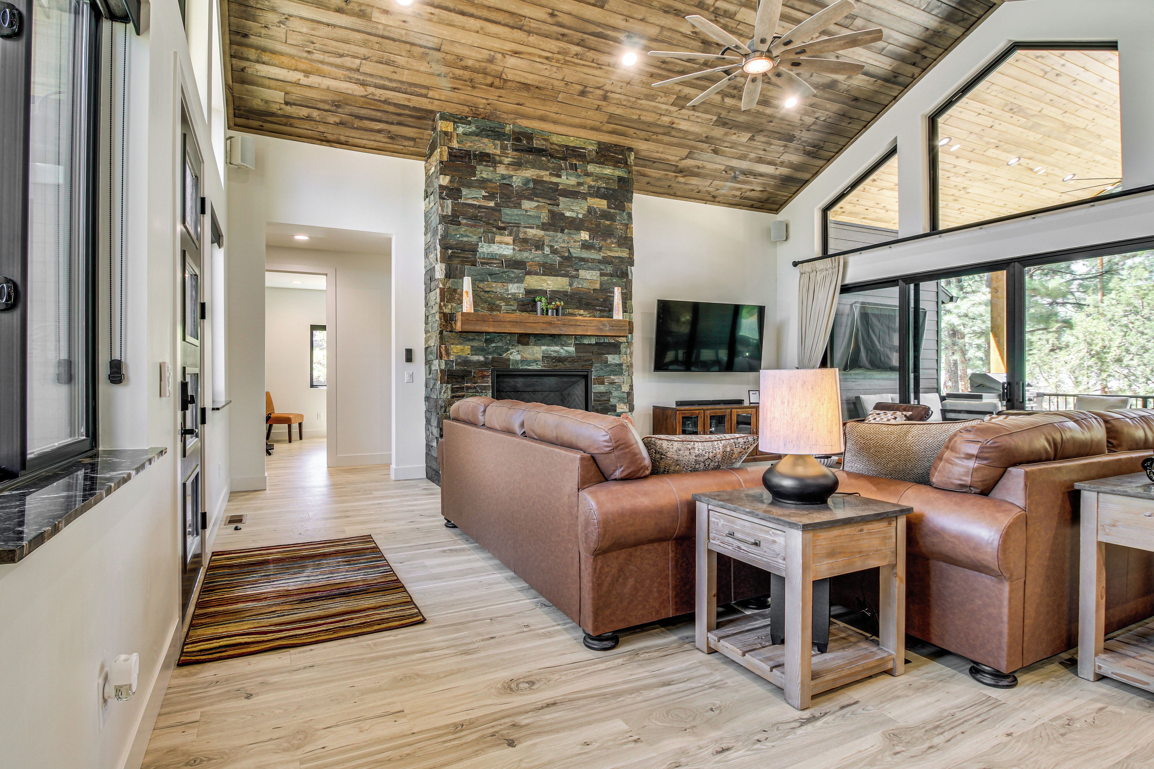 A modern living room with a stone fireplace, leather sofas, and large windows.