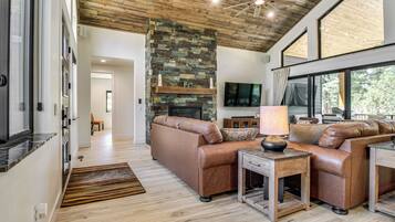 A modern living room with a stone fireplace, leather sofas, and large windows.