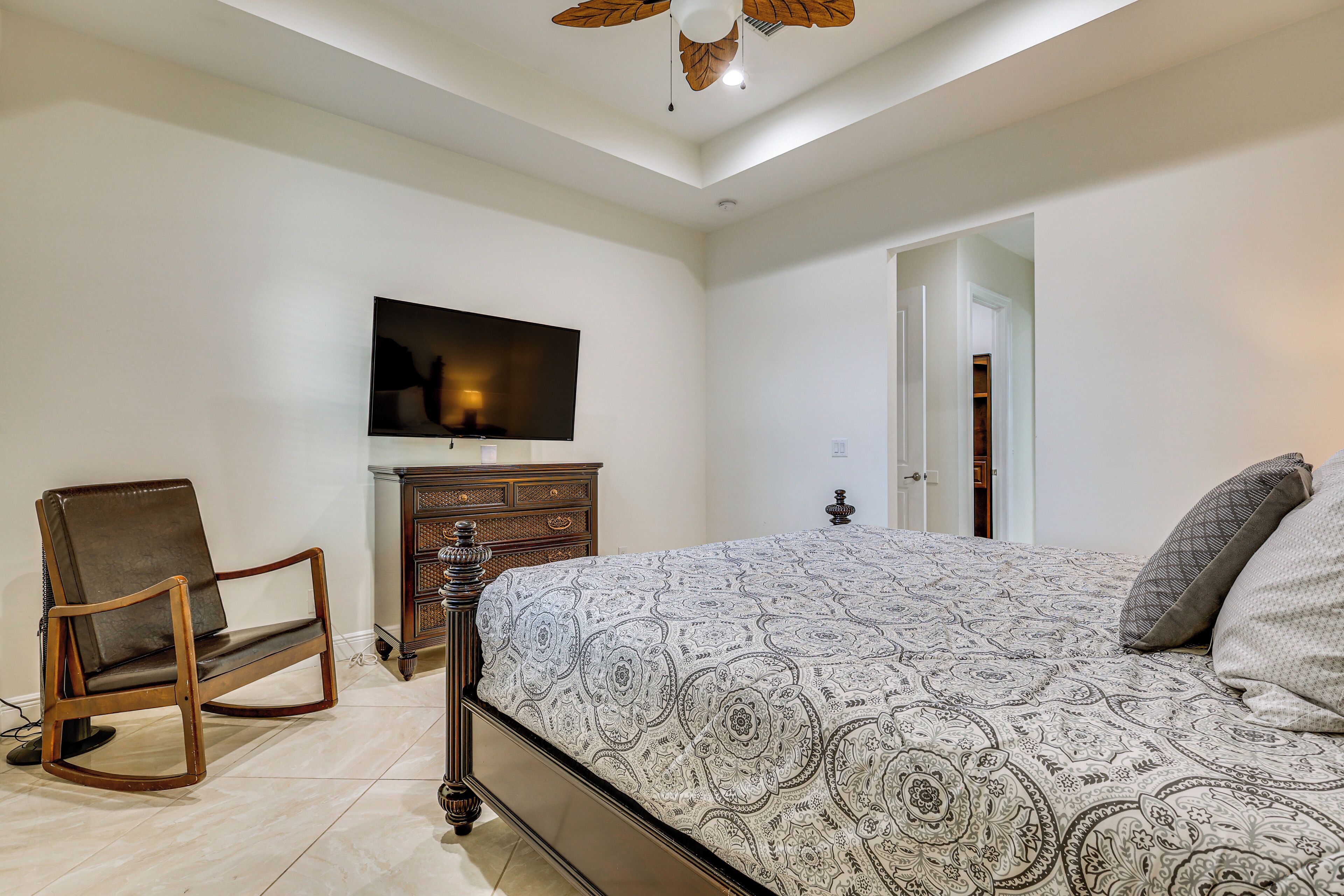 A bedroom with a bed, a television, a wooden dresser, and a rocking chair.