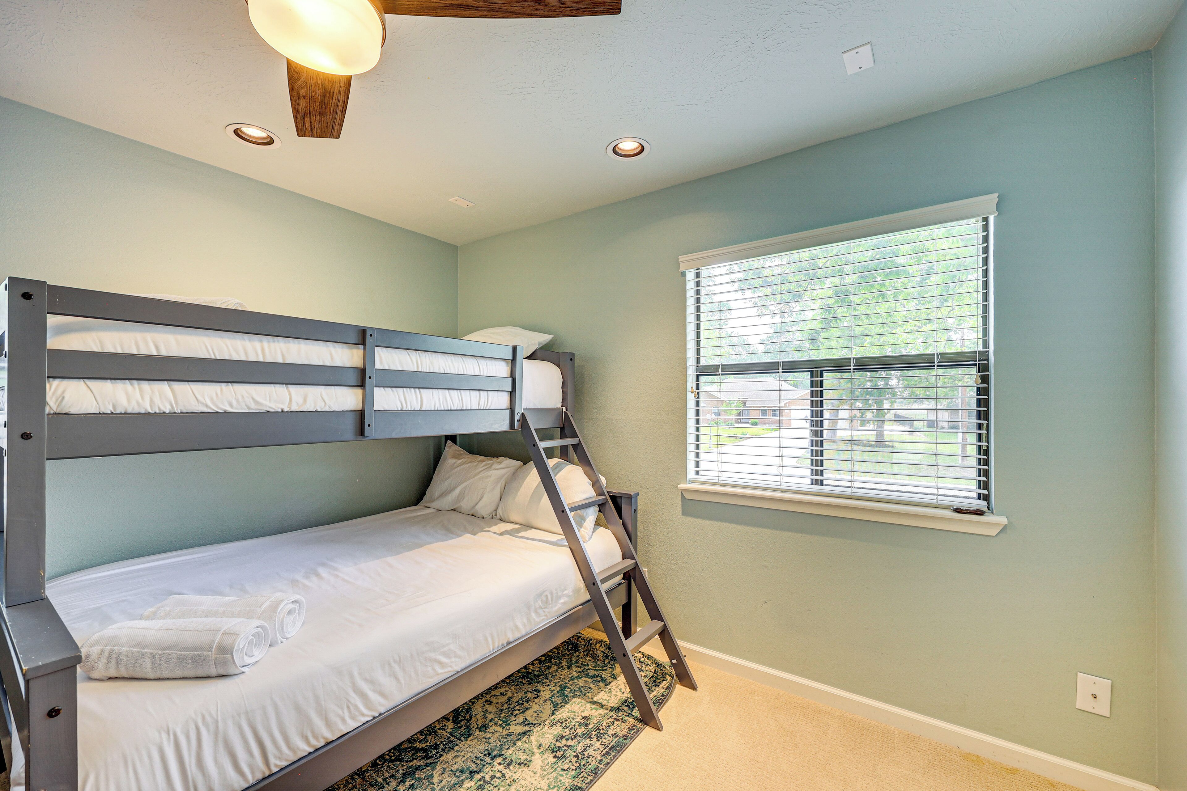 A bunk bed with a ladder, a window with blinds, and a ceiling light fixture.