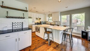 A modern kitchen with white cabinets, a wooden island with bar stools, and a built-in oven. - Waterfront Seguin Lake House Near Downtown (Seguin)