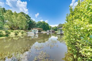 A serene riverside scene with a dock, a small building, and lush greenery. - Private Dock + Fire Pit: Serene Lake Gaston Escape (Henrico)