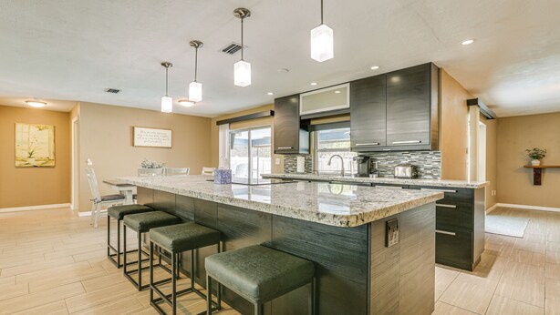 A modern kitchen with a large island, bar stools, pendant lighting, and a view of the outdoors.