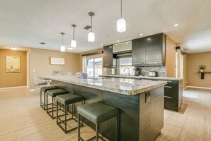 A modern kitchen with a large island, bar stools, pendant lighting, and a view of the outdoors. - Private Pool & Spacious Yard: Cape Coral Getaway (Cape Coral)