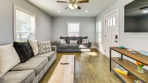 A living room with a grey sofa, a wooden coffee table, a ceiling fan, and a TV on the wall. - 3 Mi to Beach: Family Home in Corpus Christi! (Corpus Christi)