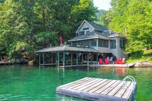 Un chalet au bord du lac, doté d’un quai, d’un espace de détente couvert avec des chaises et offrant une vue dégagée sur l’eau.