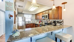 A kitchen with granite countertops, wooden cabinets, stainless steel appliances, and pendant lighting.