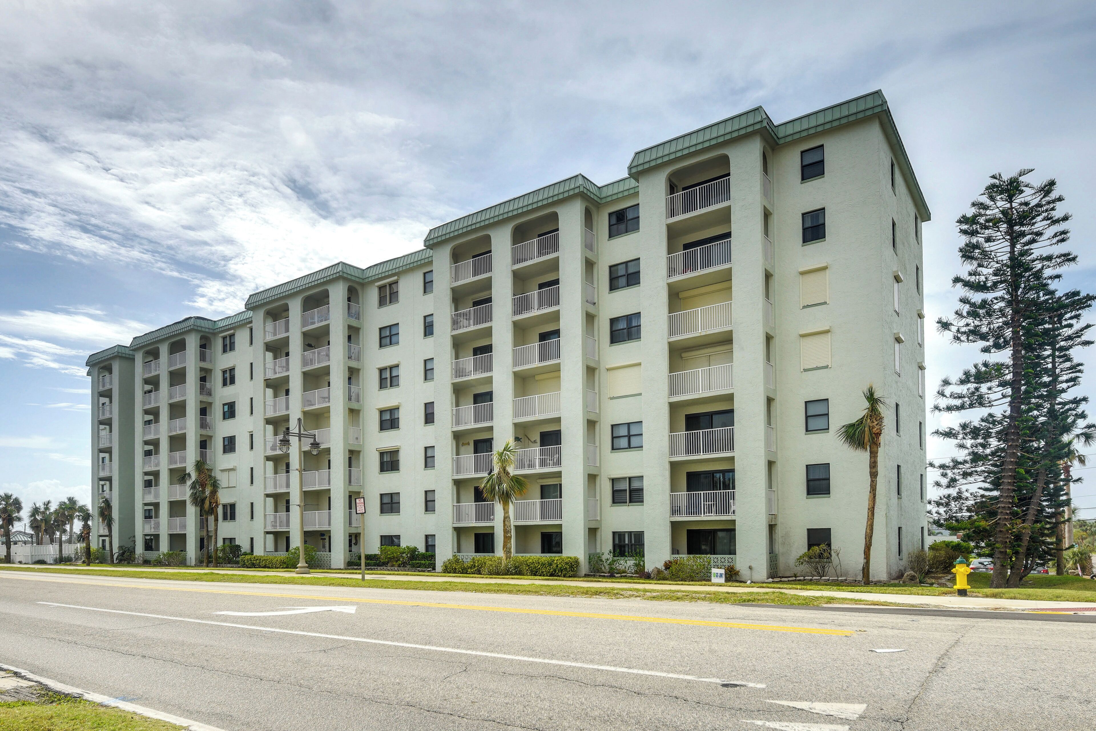 A multi-story building with balconies, a flat roof, and a street in front.