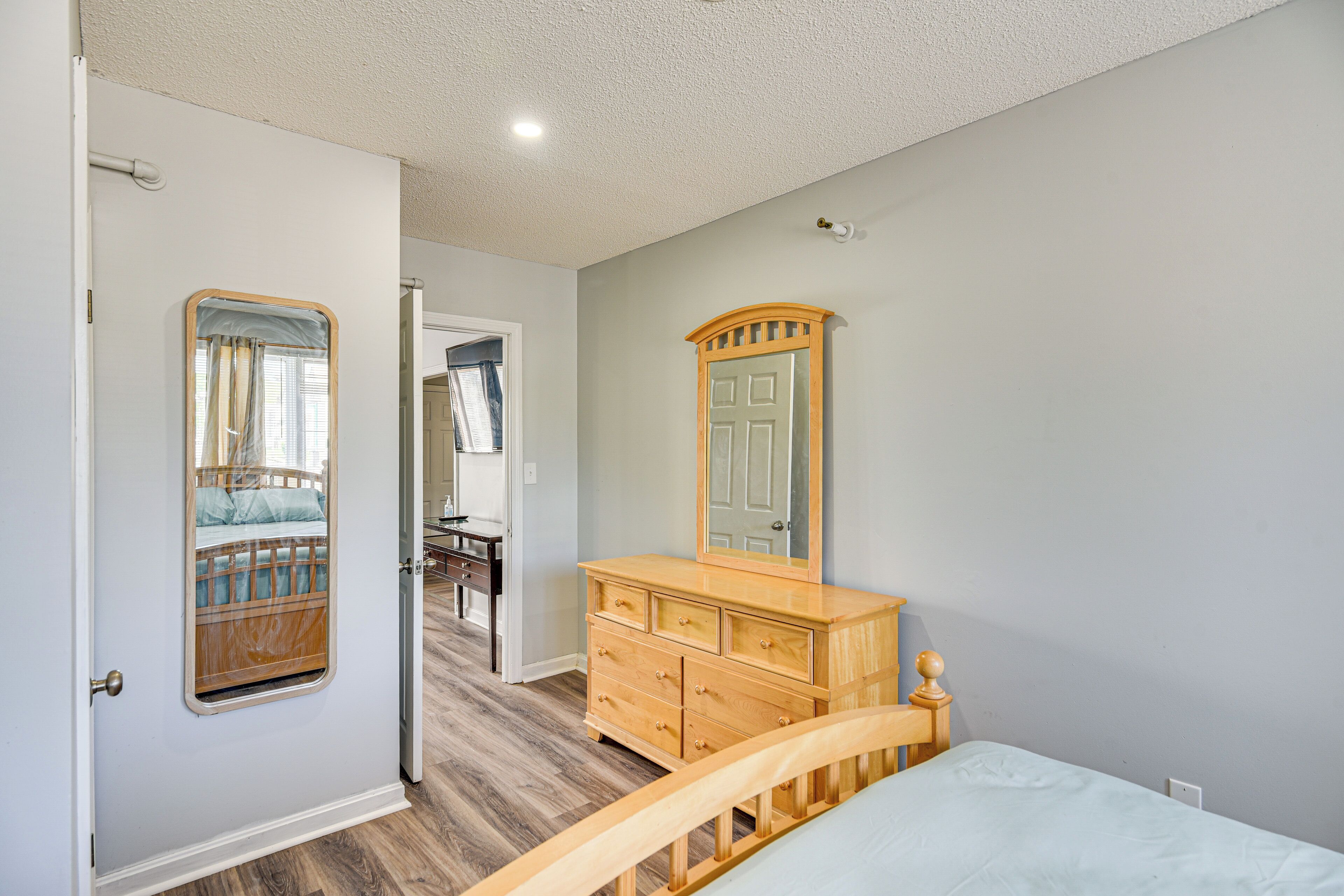 Une chambre à coucher avec un lit en bois, une commode avec un miroir et une porte donnant sur une autre pièce.
