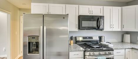 Una cocina moderna con electrodomésticos de acero inoxidable, armarios blancos y encimera de granito.