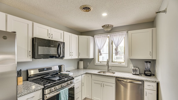 A modern kitchen with white cabinets, stainless steel appliances, a granite countertop, and a window with curtains. - 2 Mi to Waterfront: Walkable Fall River Apartment! (Fall River)