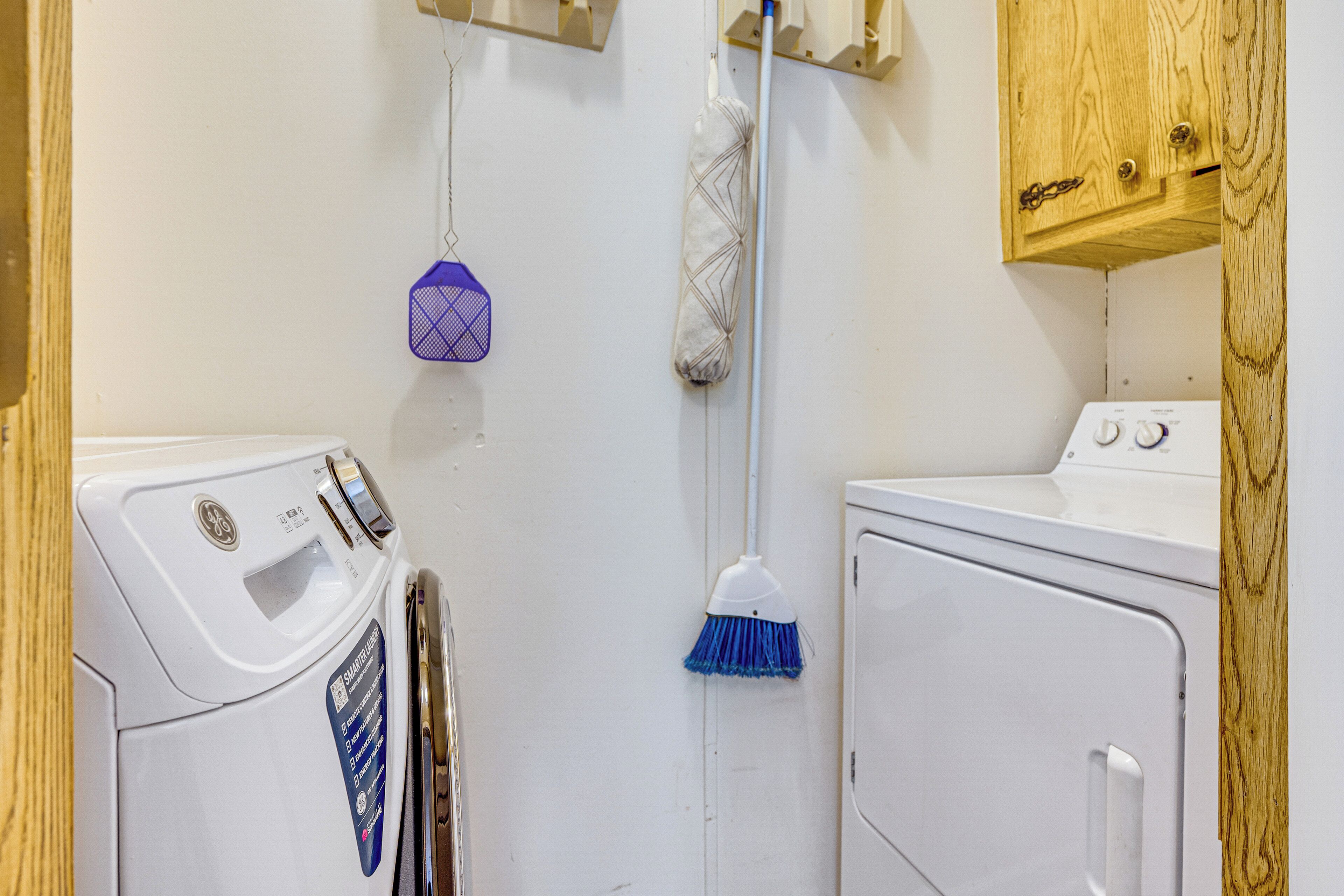 A laundry area with a front-loading washer and dryer, a mop, and a broom.