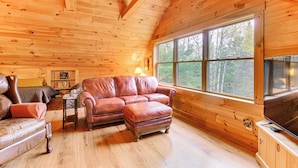 A cozy cabin interior with wooden walls, a large window, a leather sofa, and a television. - Fish, Hunt, Ride & Ski: 4-season Phillips Retreat (Phillips)
