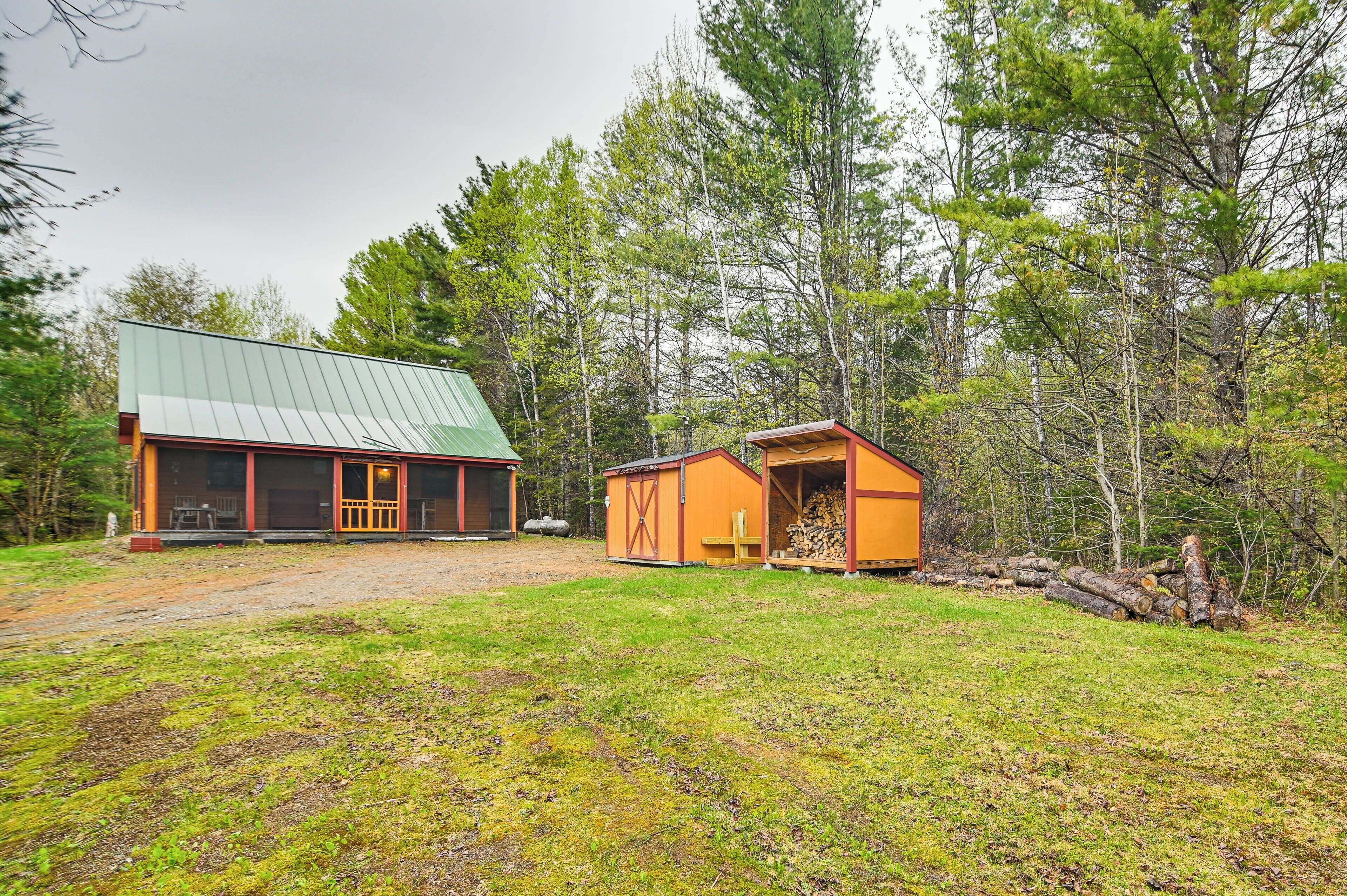 A rustic cabin with a green metal roof, a wooden deck, and a small shed with a red door.