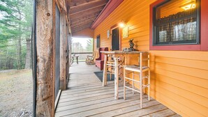 A wooden cabin with a porch, a dining table, chairs, and a window with curtains. - Fish, Hunt, Ride & Ski: 4-season Phillips Retreat (Phillips)