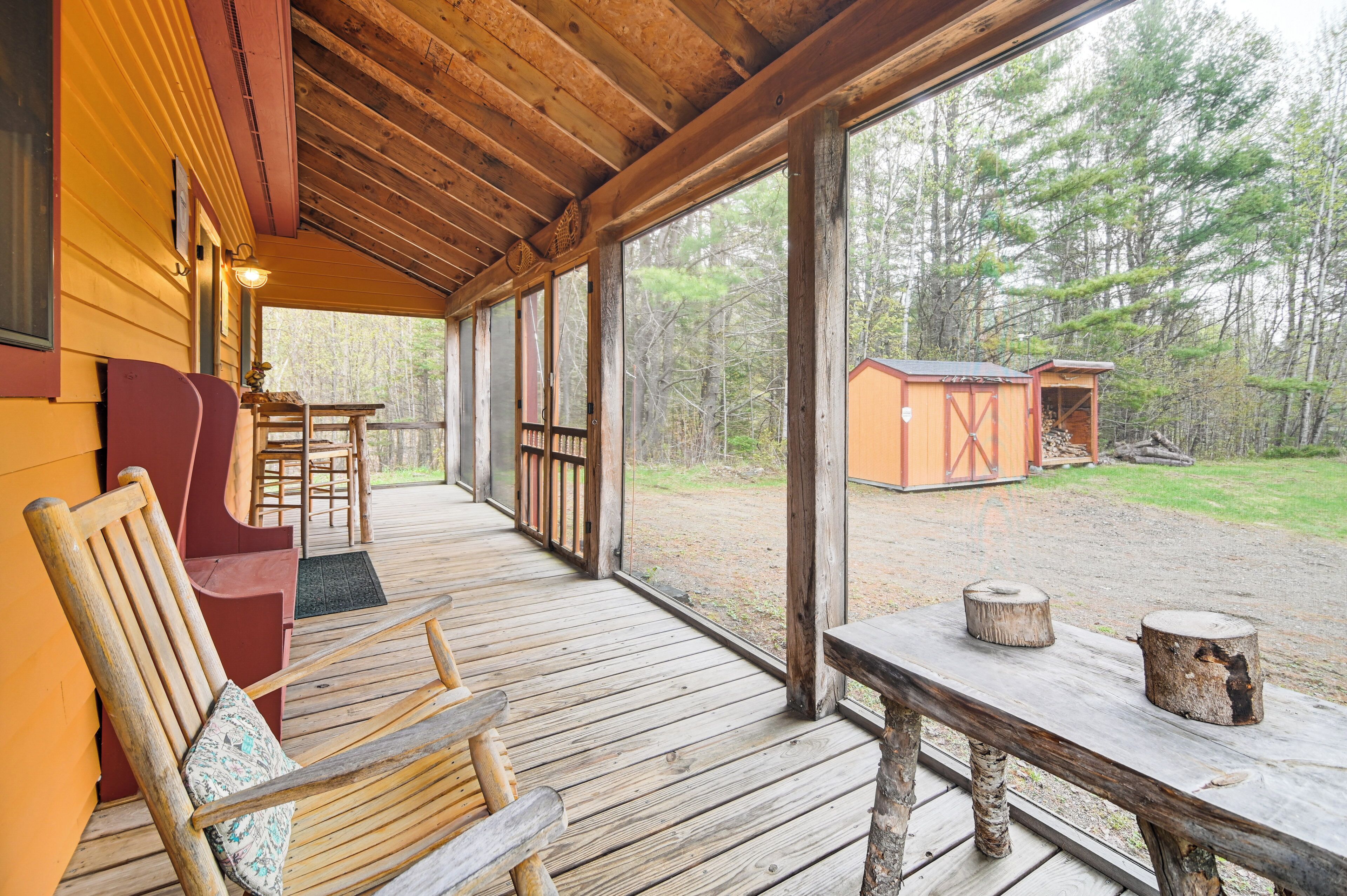 A wooden deck with a covered seating area, a small table, and a view of a forested area.