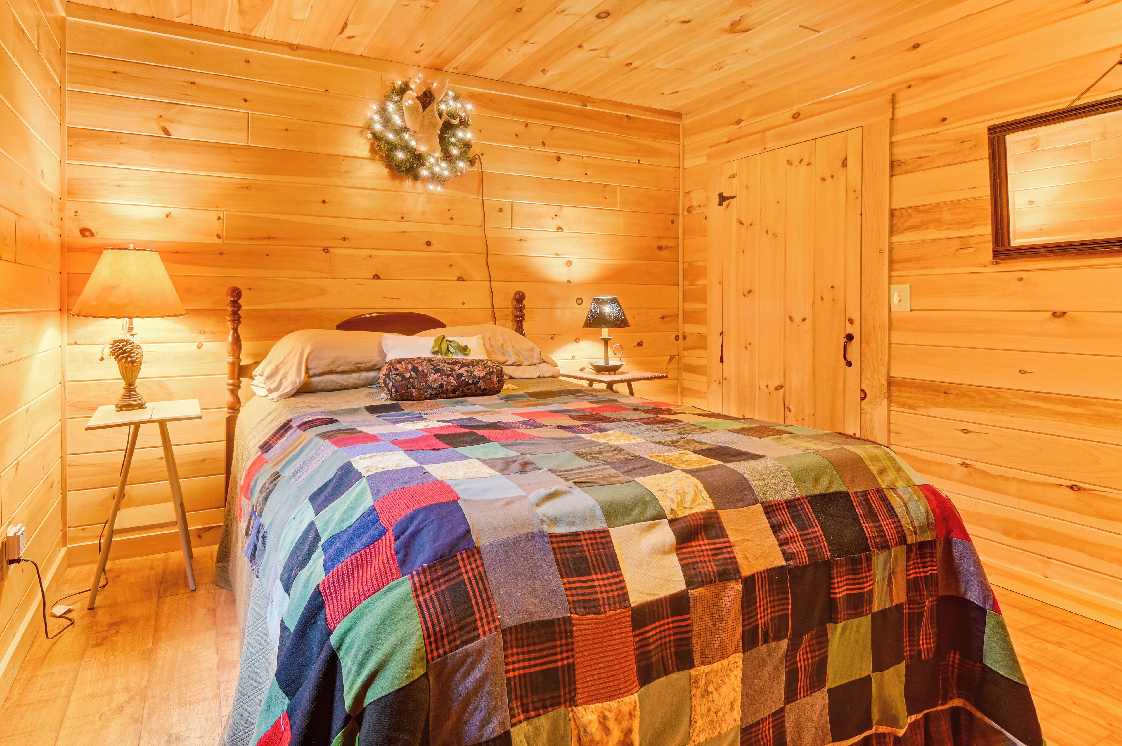Een knus slaapkamer in een houten chalet, met een bed, twee nachtkastjes, een lamp en een krans aan de muur.