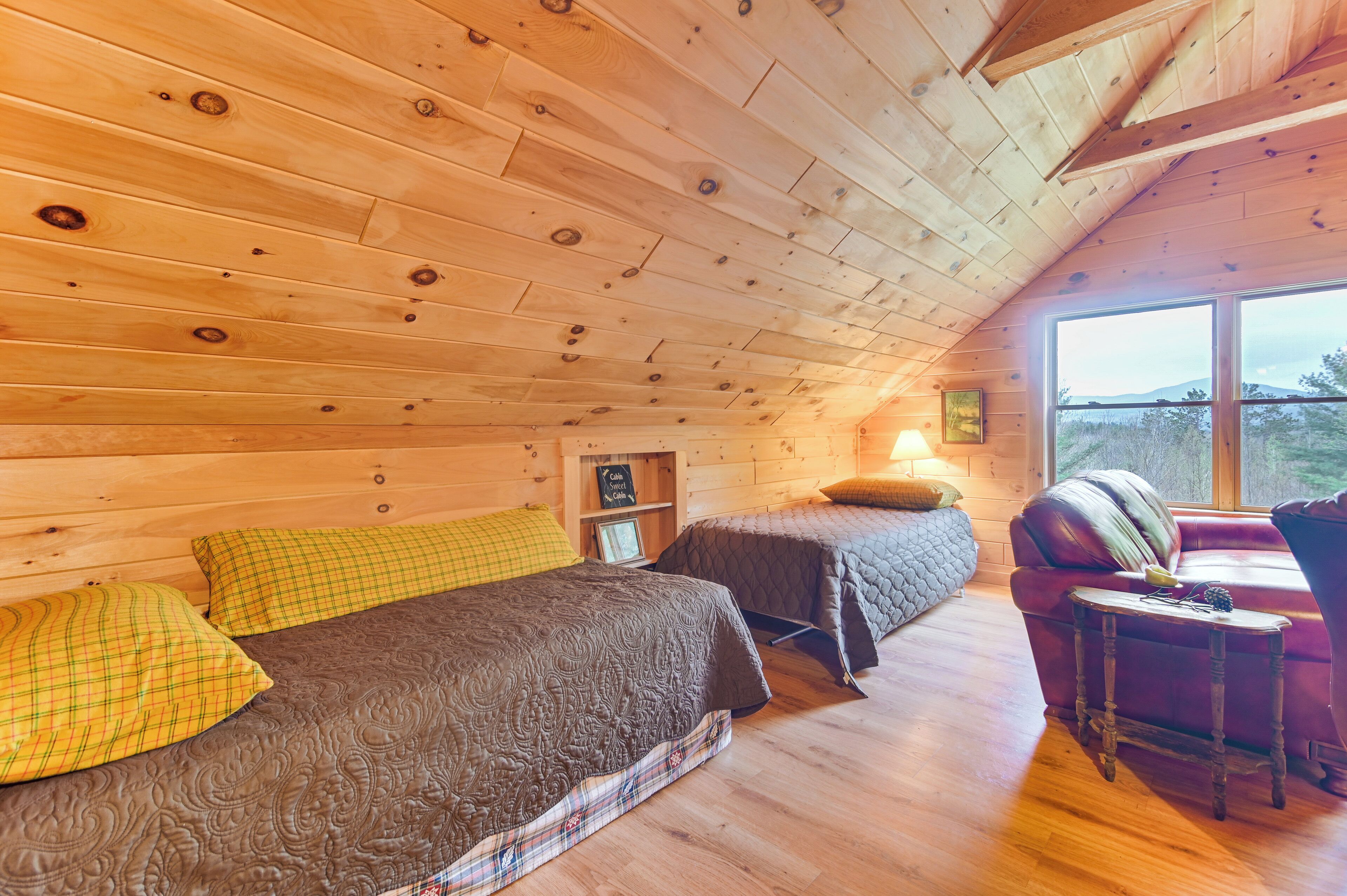 Interior acogedor de una cabaña con dos camas, techo de madera, una mesita y ventana con vistas.