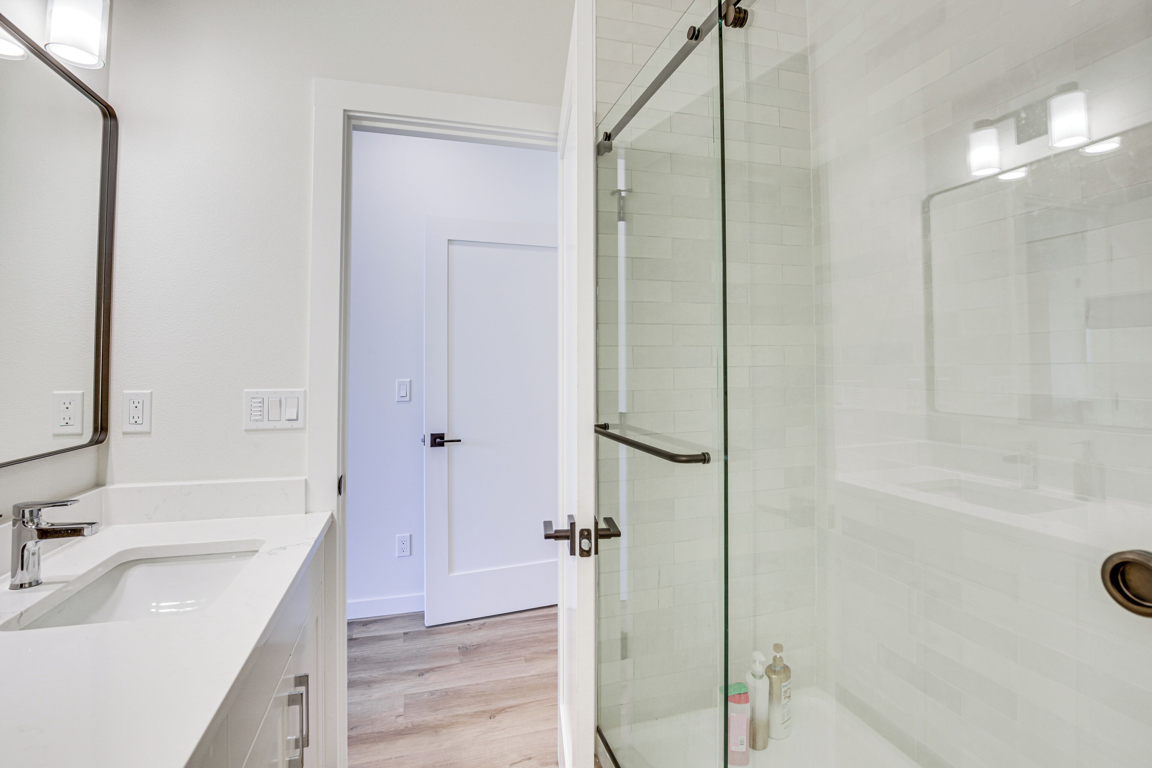 A modern bathroom with a glass shower enclosure, a white sink, and a door leading to another room.