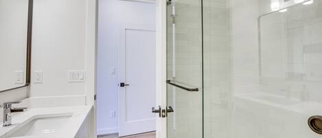 A modern bathroom with a glass shower enclosure, a white sink, and a door leading to another room.