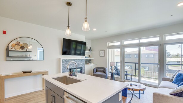 A modern kitchen with a large island, a dining area with a round table, and a balcony with a view. - Walk to Beaches: 'siletz Bay Bliss' Townhome (Lincoln City)