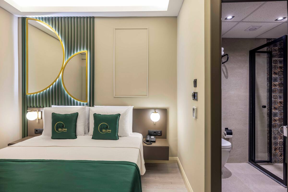 Une chambre d’hôtel comprenant un lit, des lampes de chevet, une table de nuit, un miroir et une salle de bain avec douche et toilettes.