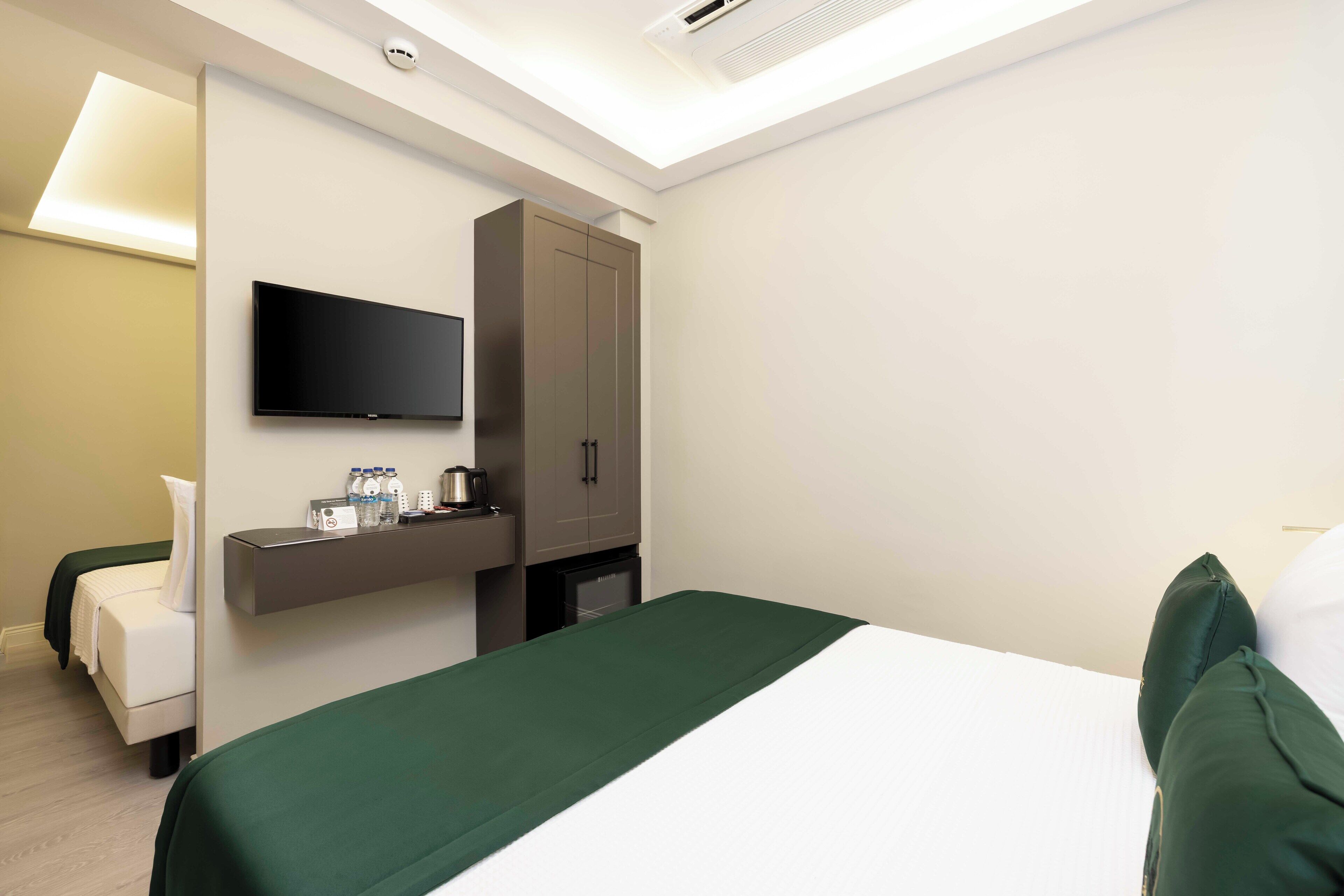 A hotel room with a bed, a TV mounted on the wall, a minibar, and a desk with a lamp.