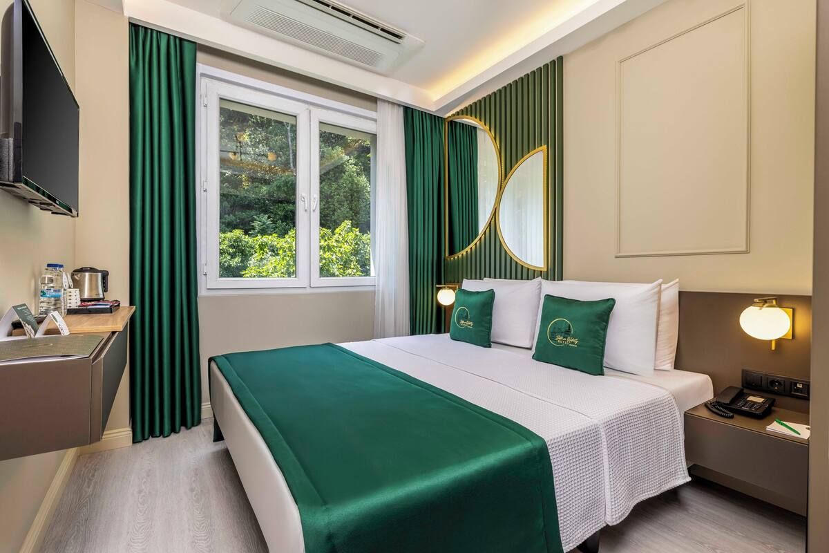 Une chambre d’hôtel avec un lit, un bureau, un téléphone et une fenêtre avec des rideaux.