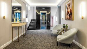 Un pasillo moderno con suelo alfombrado, un muro espejado, una escalera y un sillón blanco.
