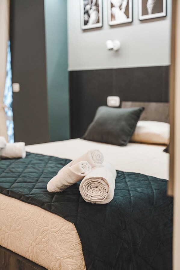 A neatly made bed with a dark green quilt, a rolled-up towel, and a pillow. - Monteverde Vatican (Rome)