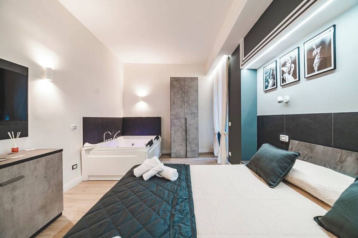 Un dormitorio moderno con una cama grande, una bañera integrada y un televisor de pantalla plana.