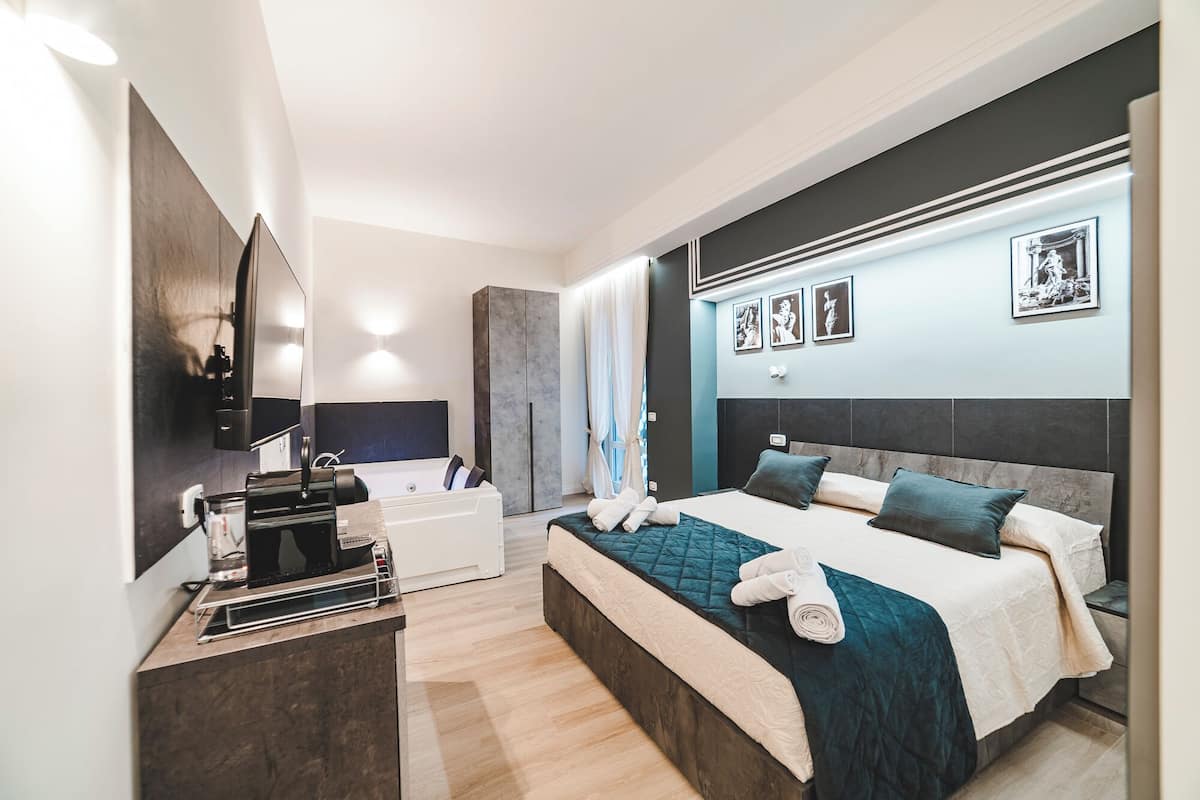 Una habitación de hotel moderna con una cama grande, una mesita de noche, un espejo y un televisor fijado a la pared.