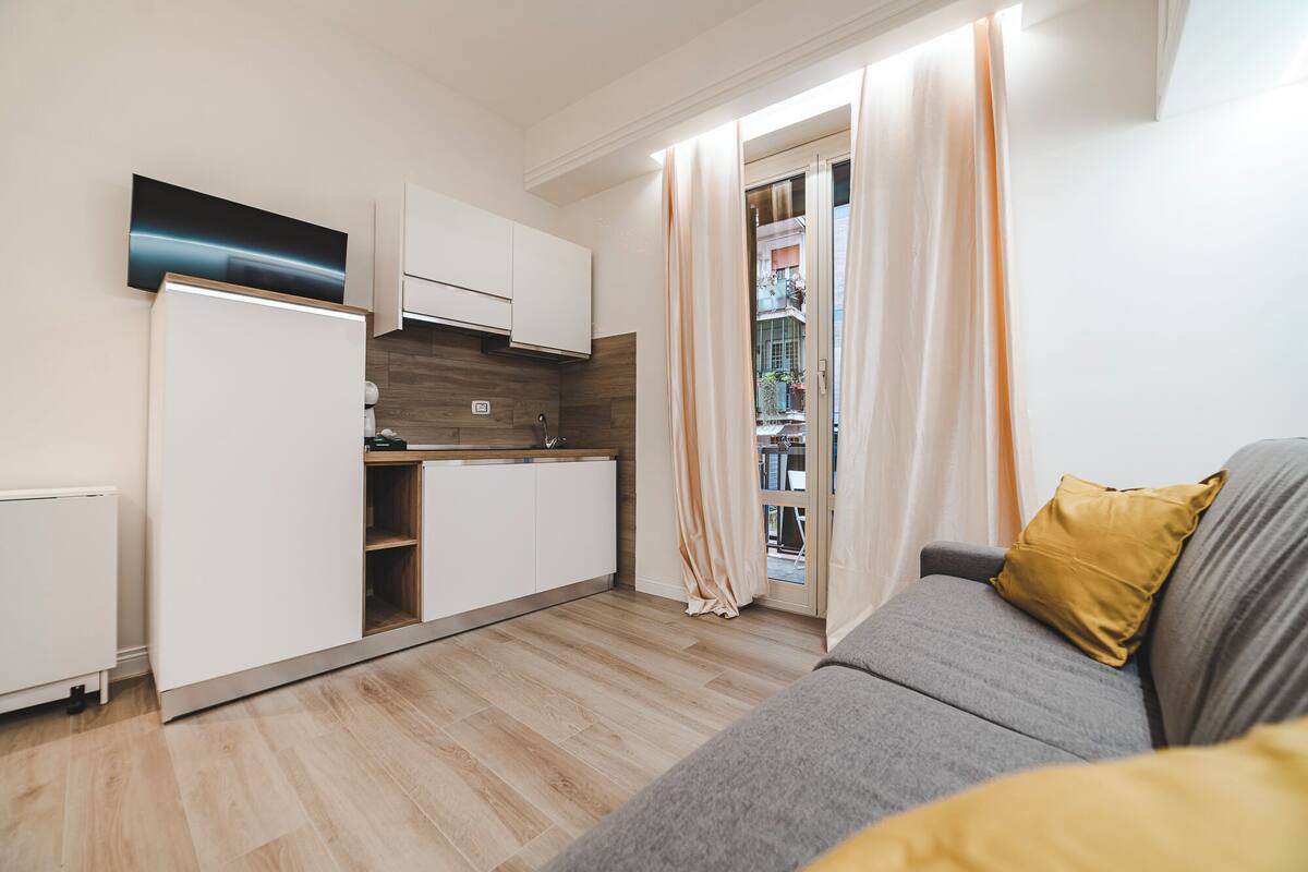 Un espacio habitable compacto con kitchenette, un sofá y una puerta corrediza de vidrio que da a un área exterior.